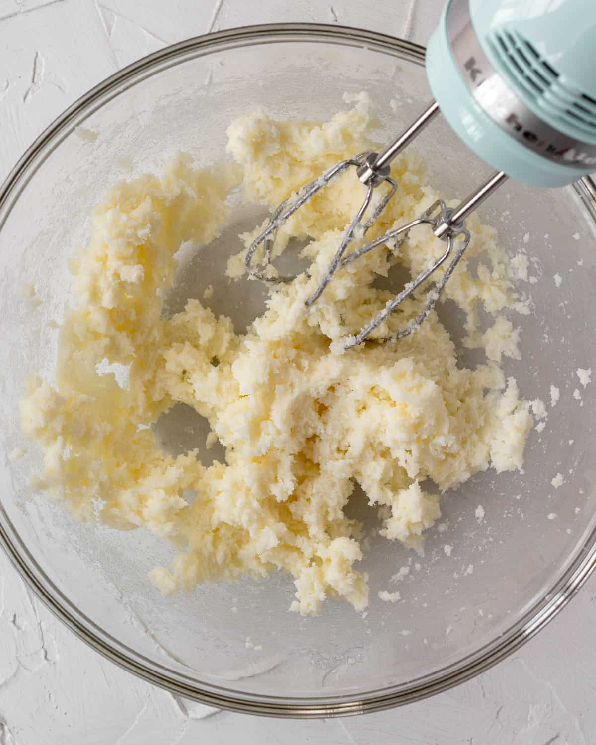 clear glass bowl with butter and sugar mixed together by an electric mixer
