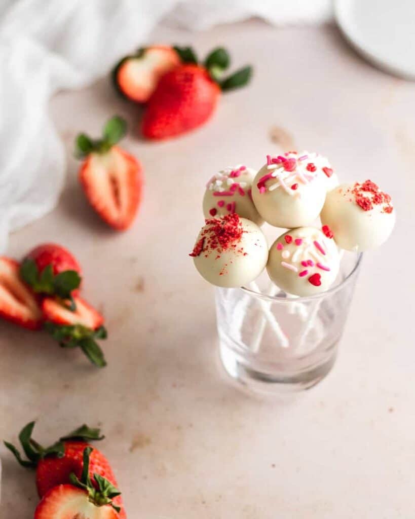 Cake pops bunched together inside glass dish with strawberries 