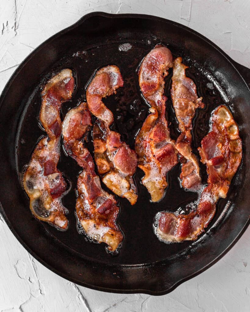 bacon frying in a black cast iron skillet