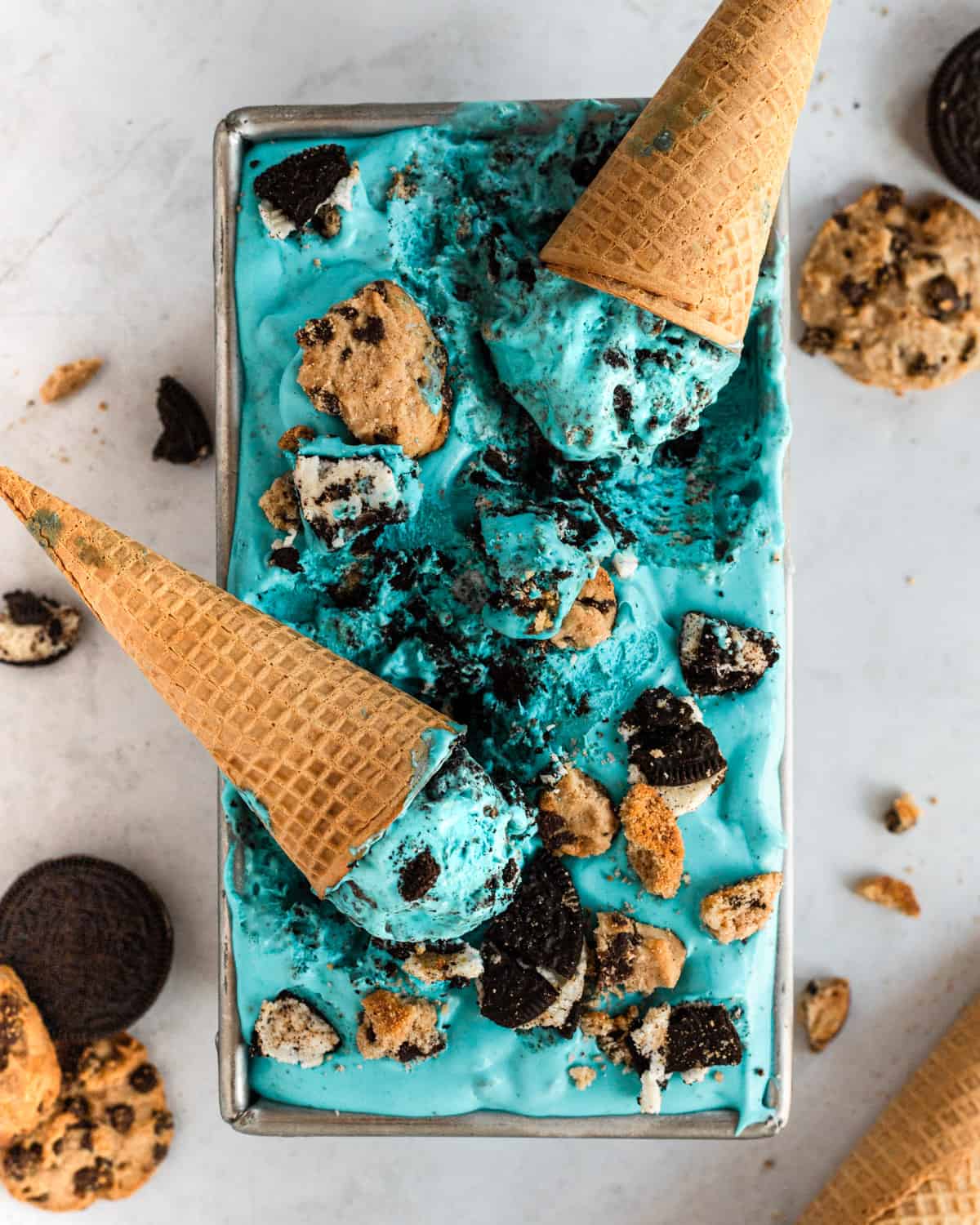 cookie monster ice cream in a rectangular pan with cones and crumbled cookies on top and laying around it. 