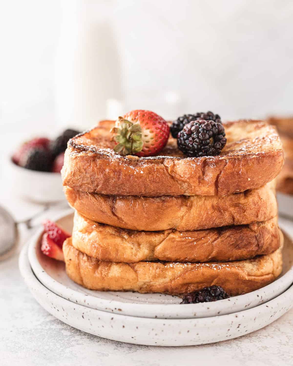 stack of french toast on a plate with berries on top and in the background
