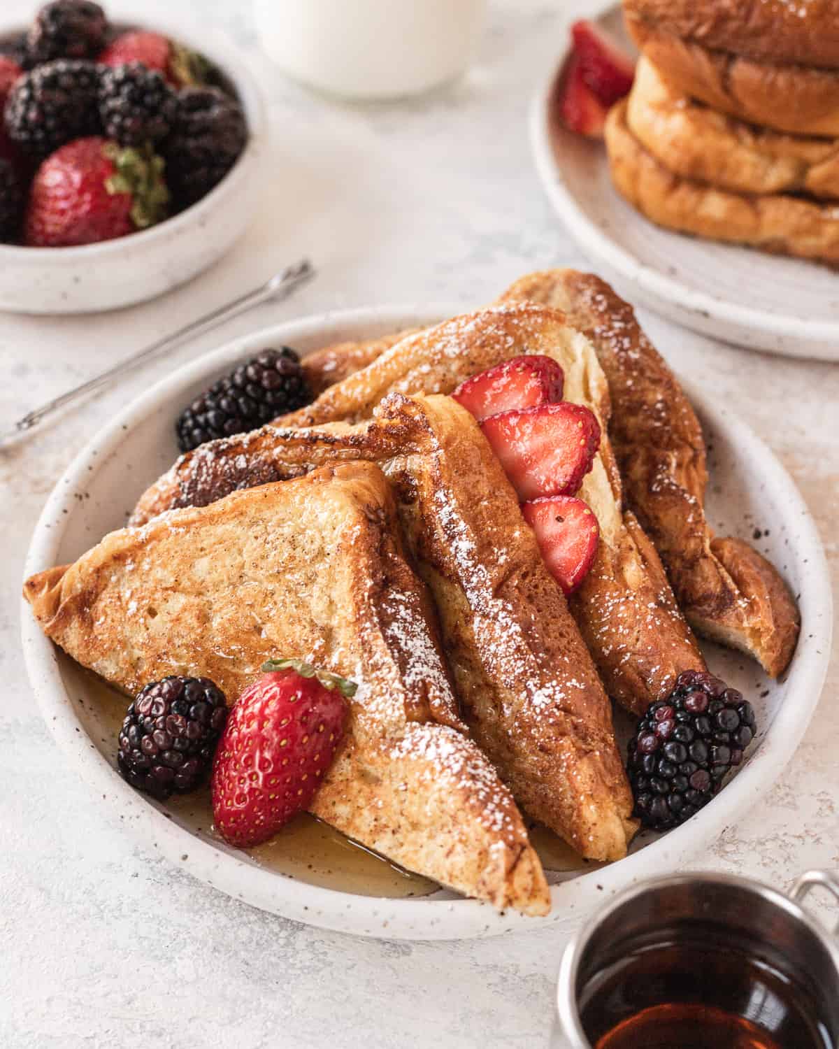 short stack of french toast on a plate with berries and maple syrup on top