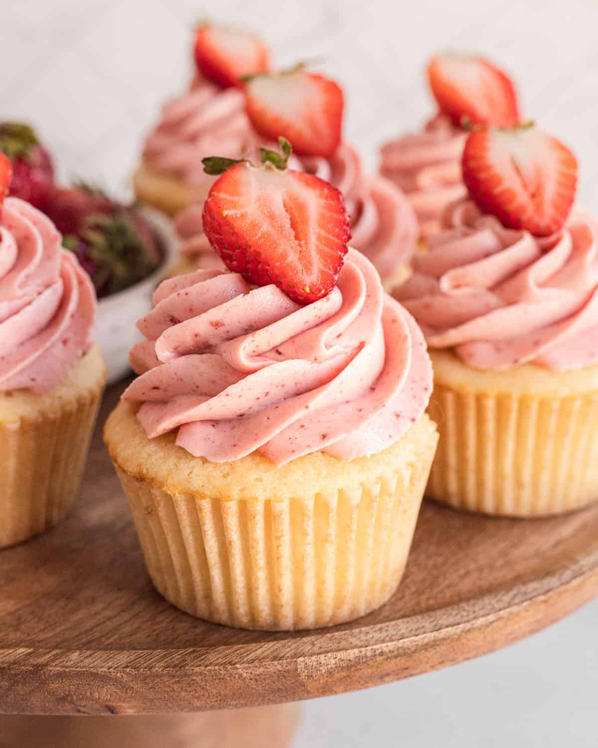 group of strawberry cupcakes sitting on a wooden cake stand