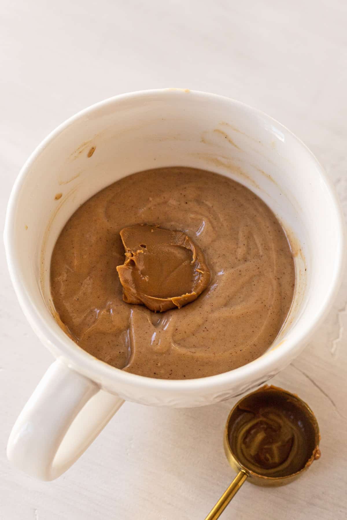 mug cake batter in the mug with a tablespoon of cookie butter on top before baking it
