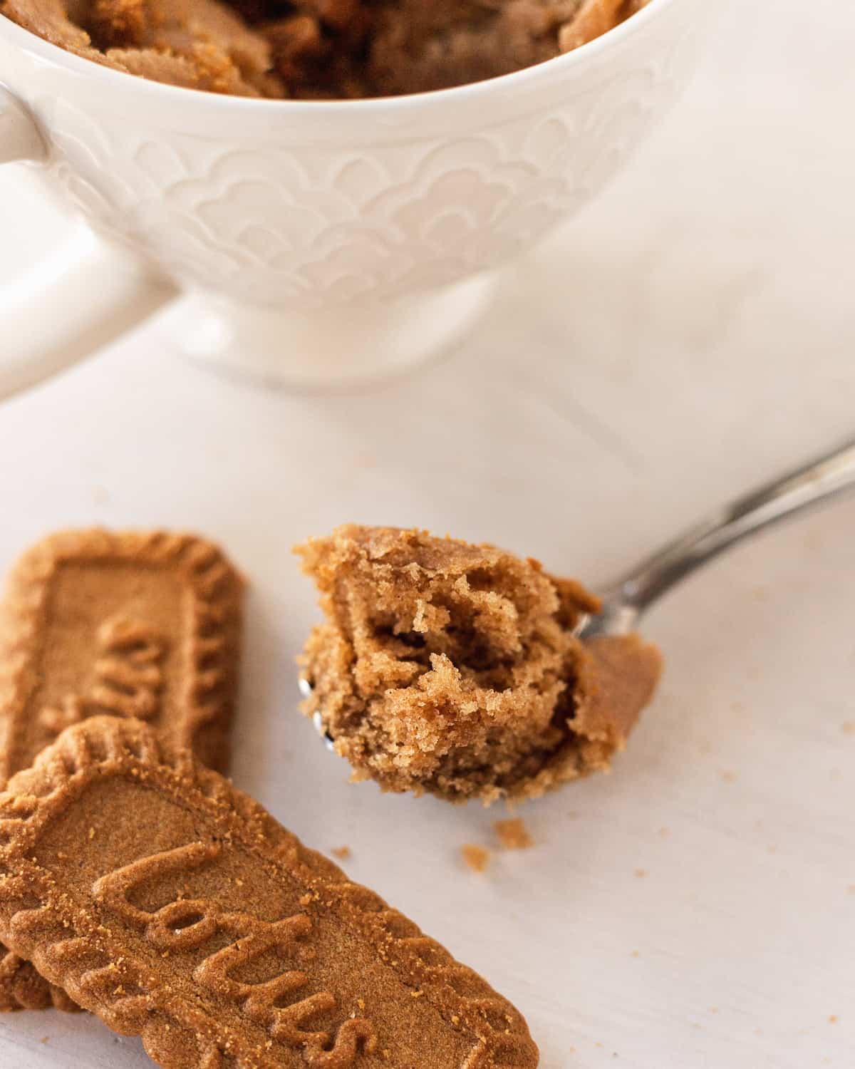close up shot of a scoop of biscoff mug cake on a spoon next to biscoff cookies
