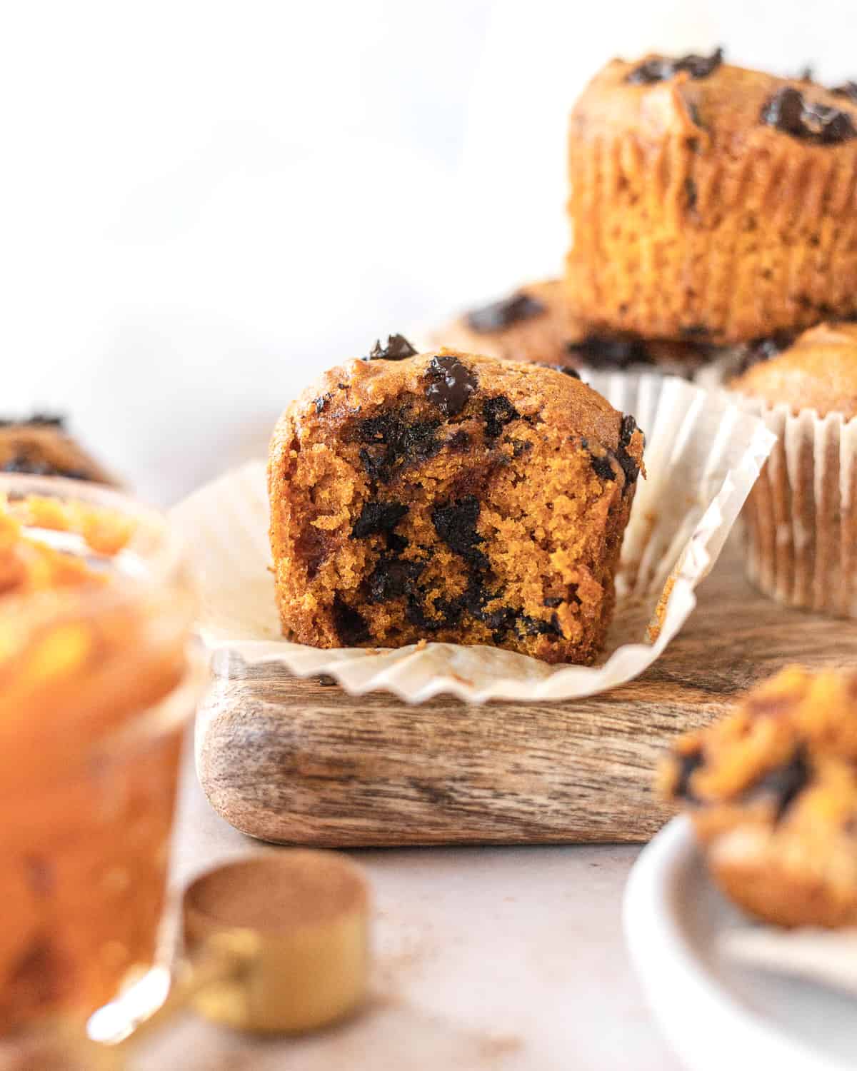 pumpkin chocolate chip muffin with a bite taken out of it on a board with muffins surrounding it 