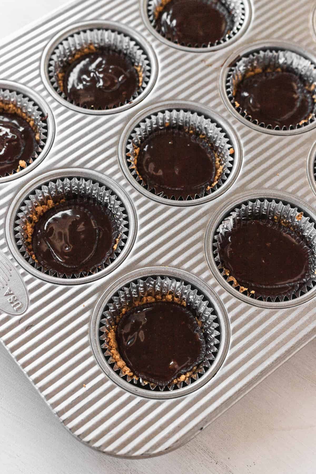 chocolate poured into the graham cracker crust in a cupcake pan