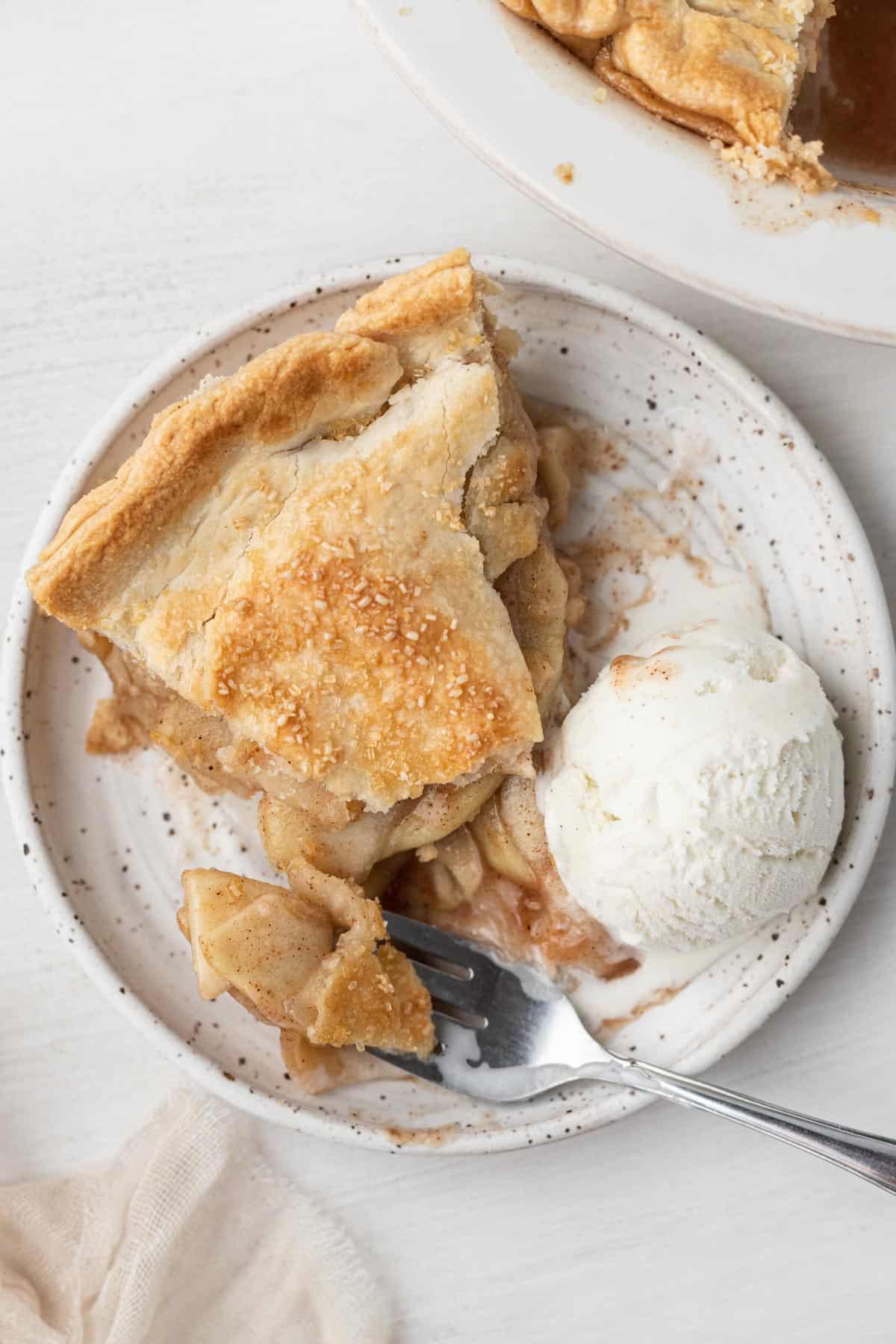 pie on white plate with a scoop of vanilla ice cream and a fork with a bite on it. 