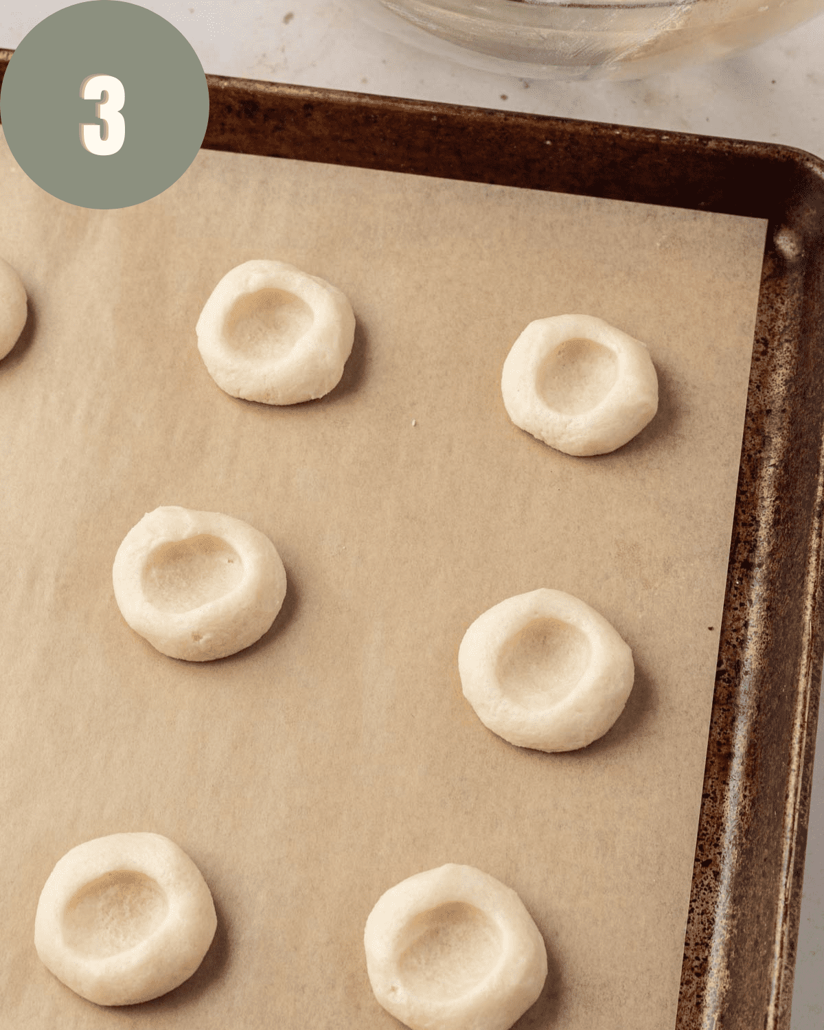 cookies on baking sheet with thumbprints pressed into it