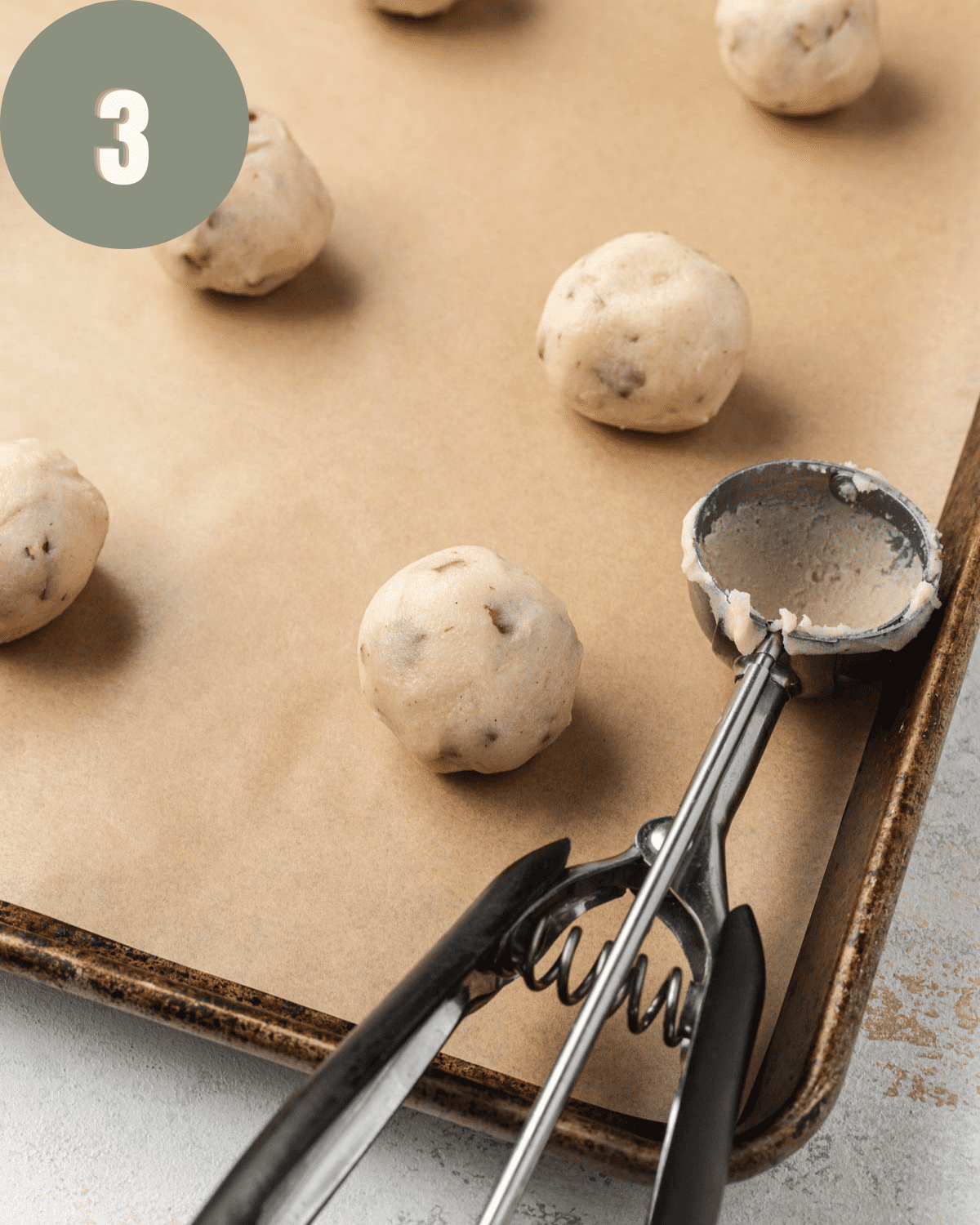cookies rolled on a baking sheet next to a cookie scoop