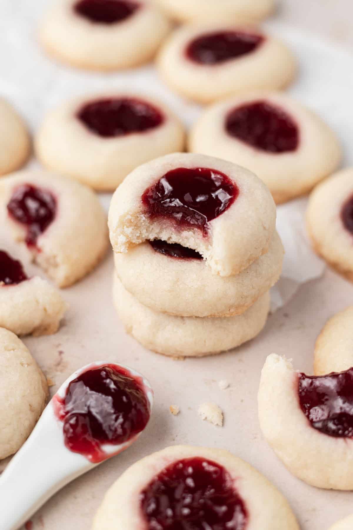 stack of 3 cookies with the top one missing a bite, surrounding by other cookies and spoon of jam