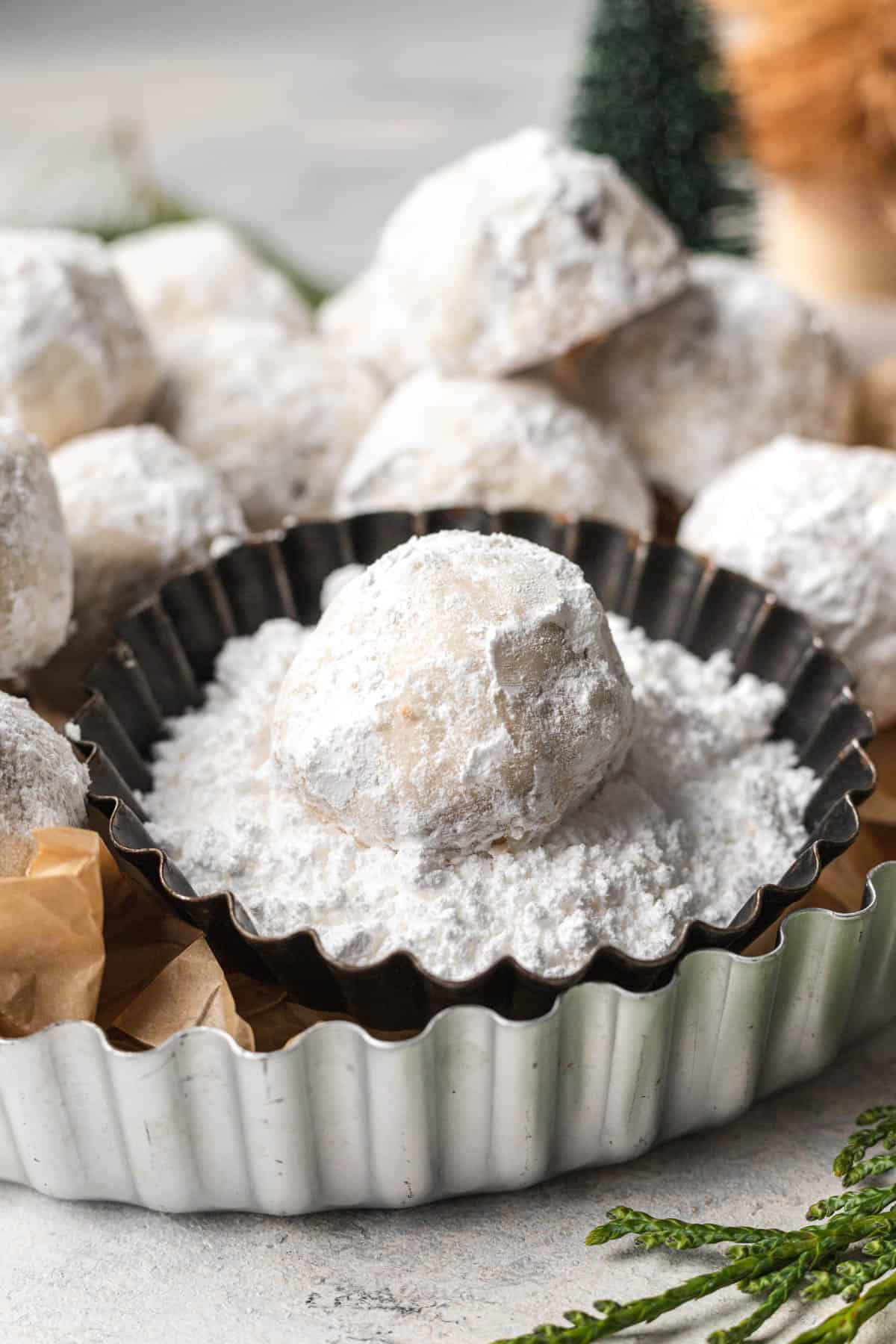 cookies in a silver tin with one cookie sitting in a bowl of powdered sugar. 