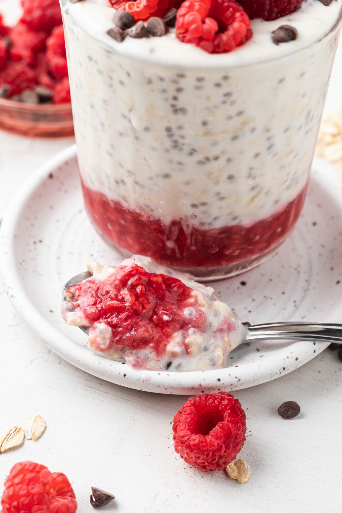 spoonful of overnight oats on a white plate with raspberries, oats, and chocolate chips sprinkled around. 