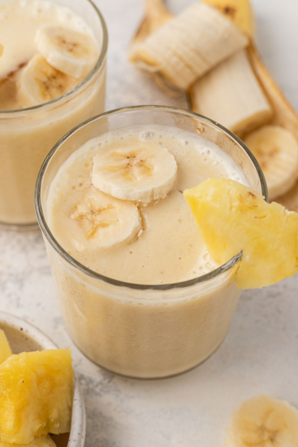 pineapple banana smoothie in a clear glass with sliced banana and pineapple on top