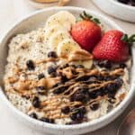 protein oats with berries and drizzled peanut butter on top in a white bowl.