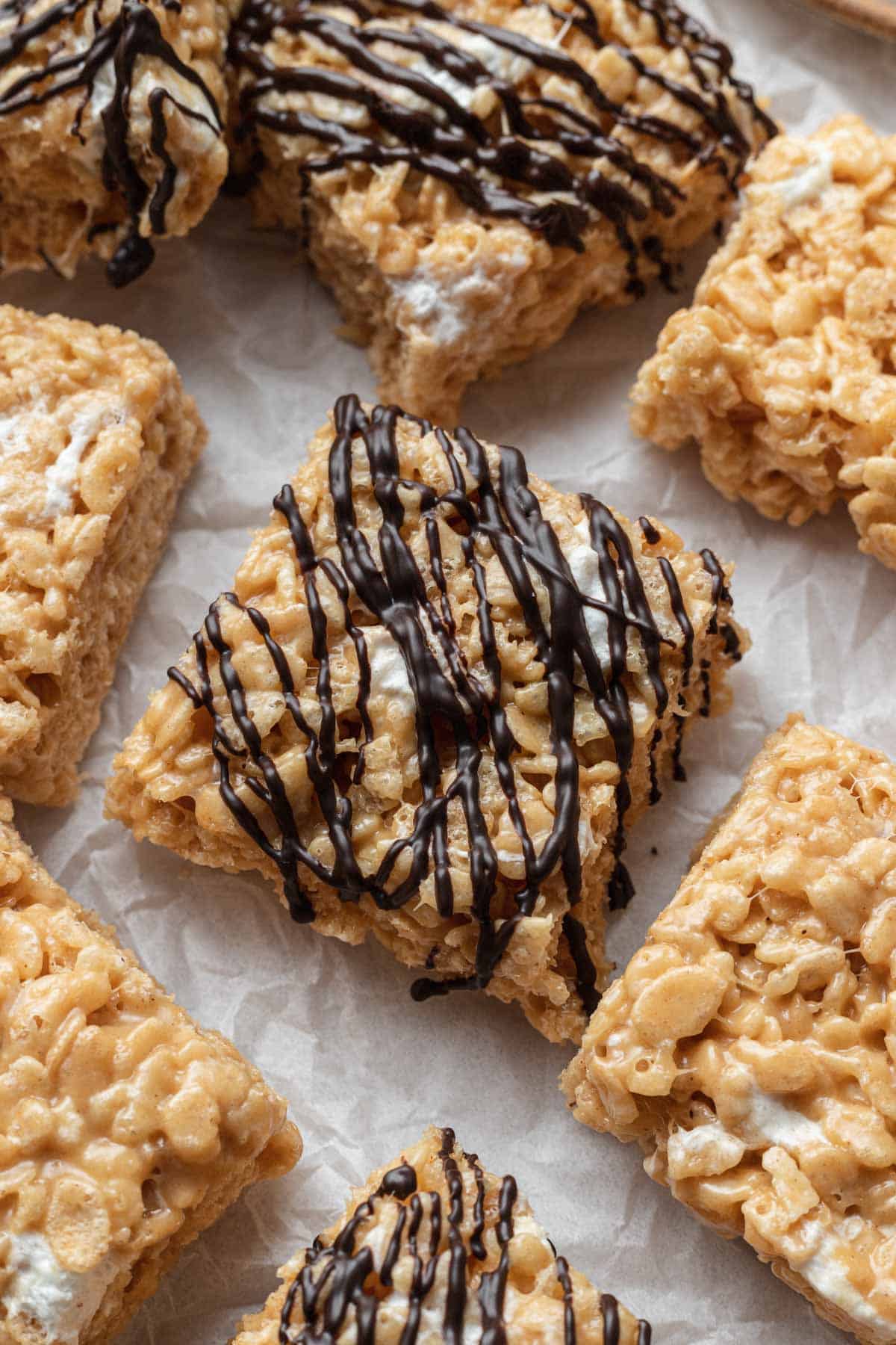 rice krispie treats on parchment paper with a chocolate drizzle over top one of them 