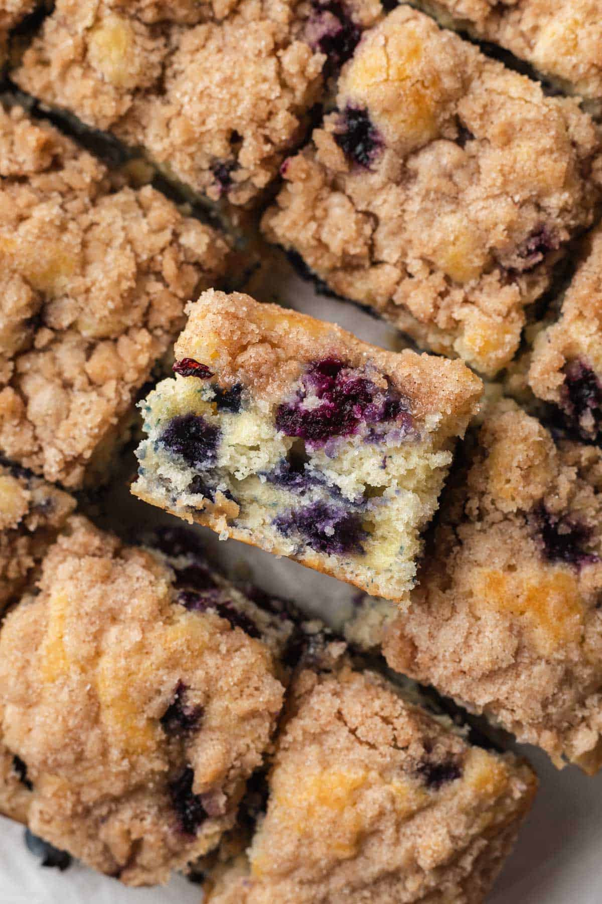 close up of a piece of blueberry buckle coffee cake on it's side surrounded by cut pieces of cake