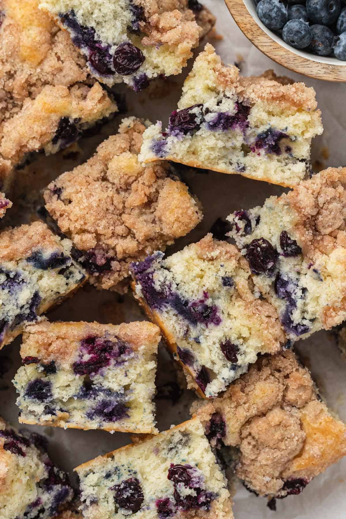 piece of cake laid out on parchment paper with juicy blueberries and crumbly topping. 
