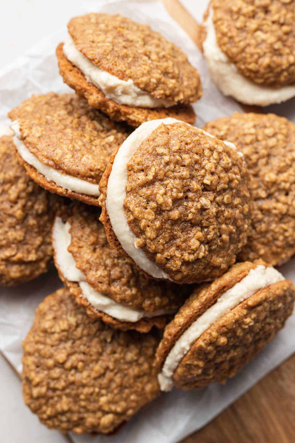 a pile of oatmeal creme pie cookies stacked on one another on a parchment paper-lined board. 