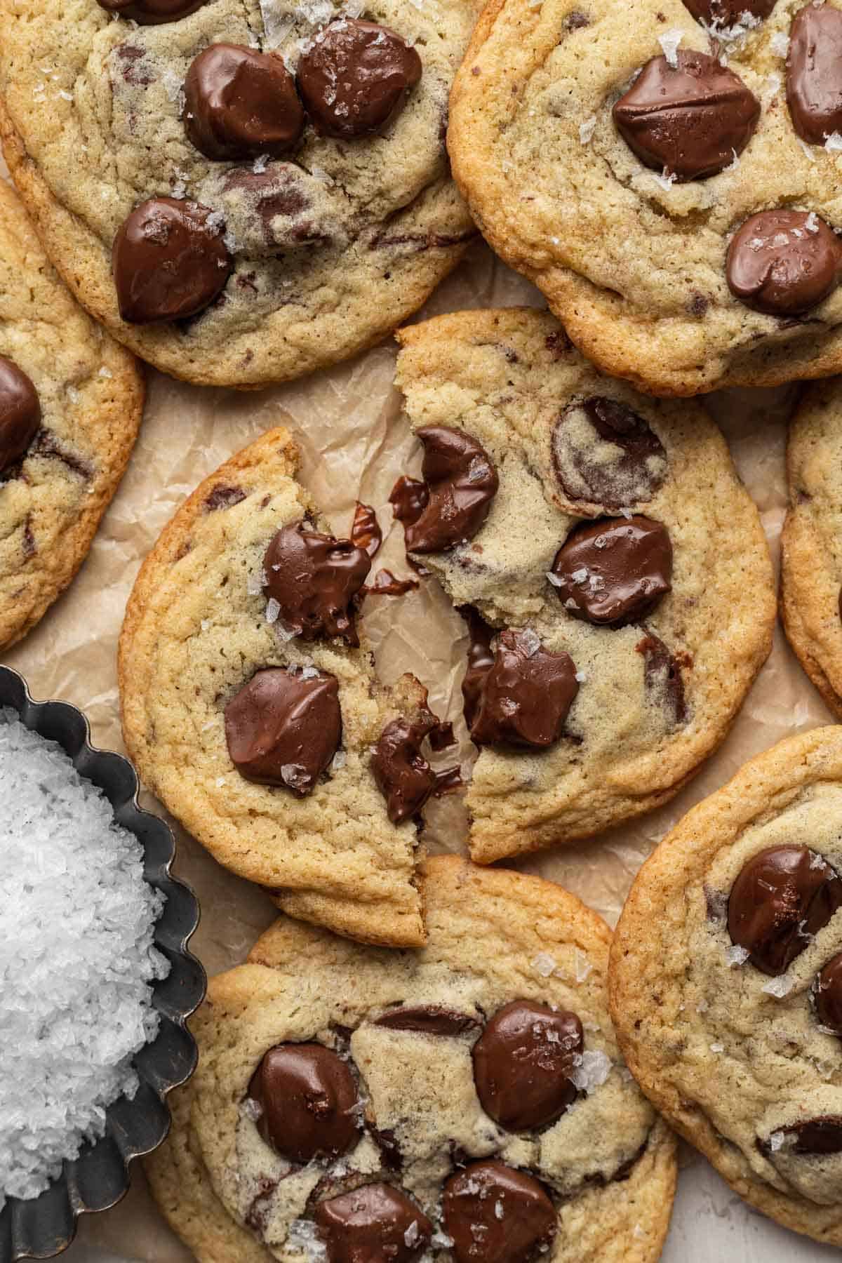 close up of cookie broken in half with gooey chocolate next to a bowl of sea salt. 