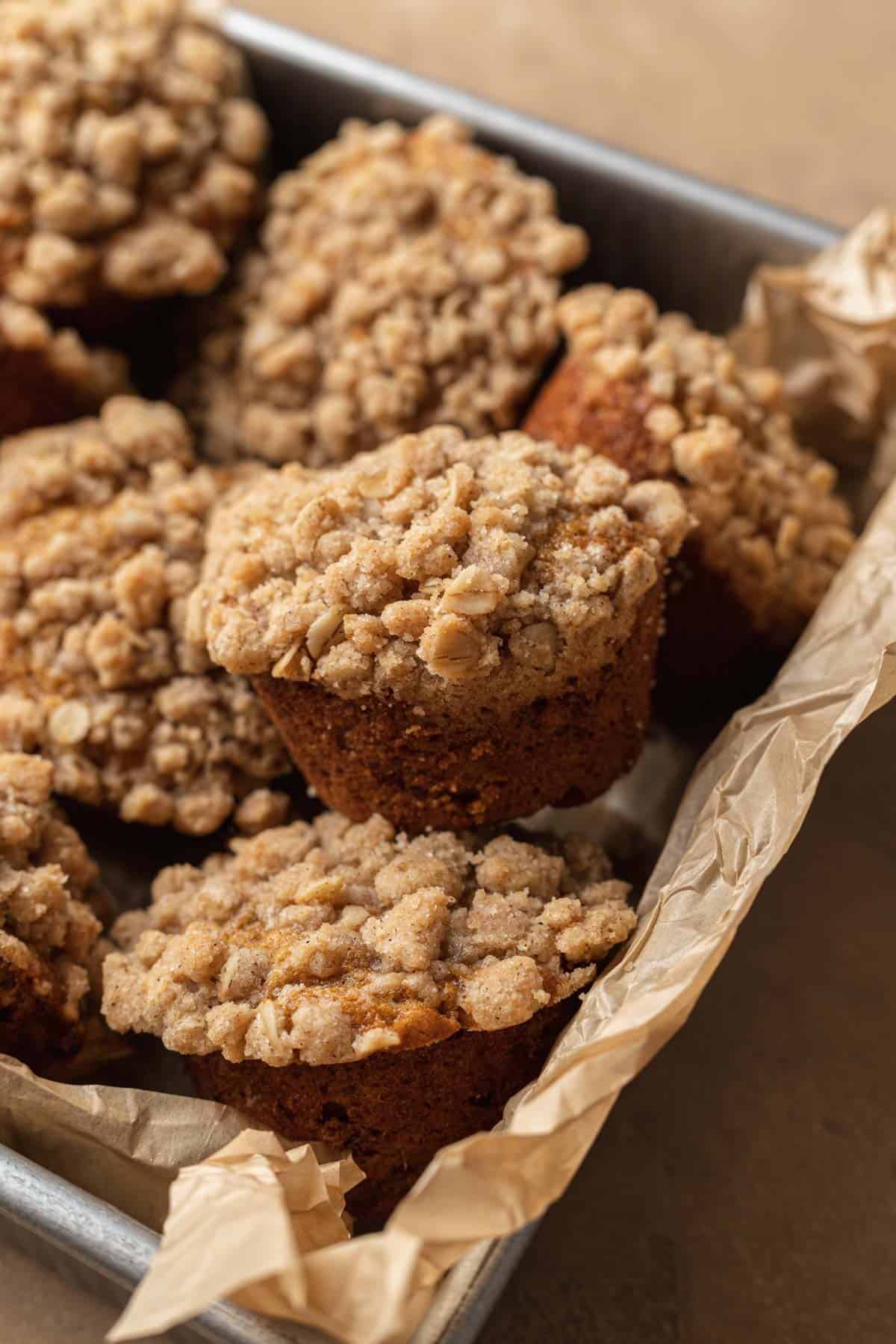 Pumpkin Banana muffins staked on top of one another in a baking pan lined with parchment paper.