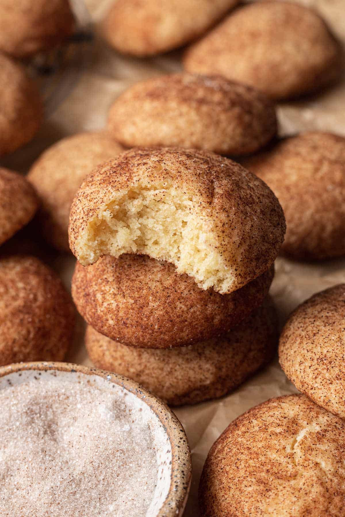Snickerdoodle cookies on baking sheet, with three snickerdoodle cookies stacked on top of each other and the top cookie having a bite out of it.