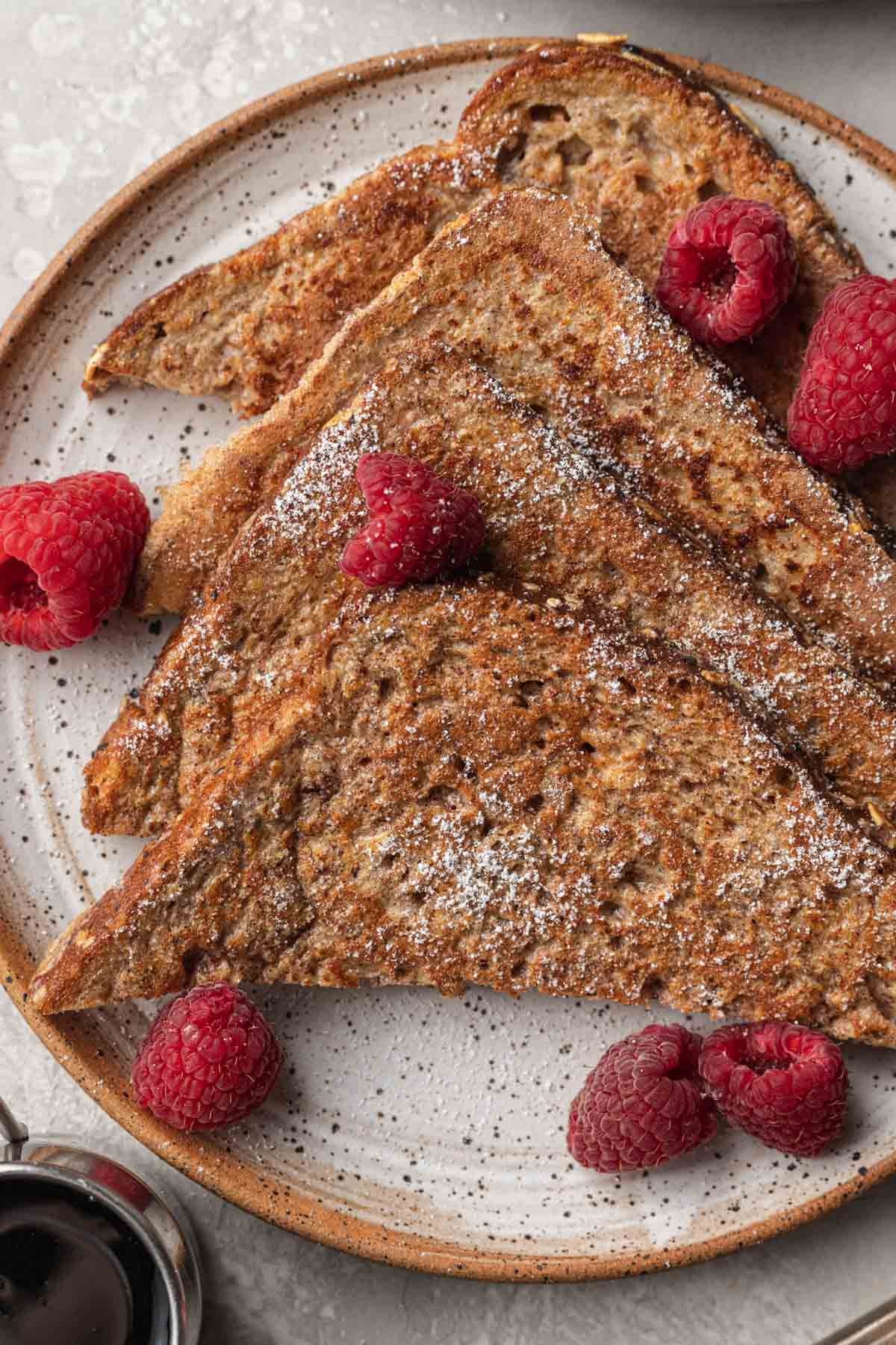 Ready to eat protein french toast on a plate topped with fresh raspberries and dusted with powdered sugar.