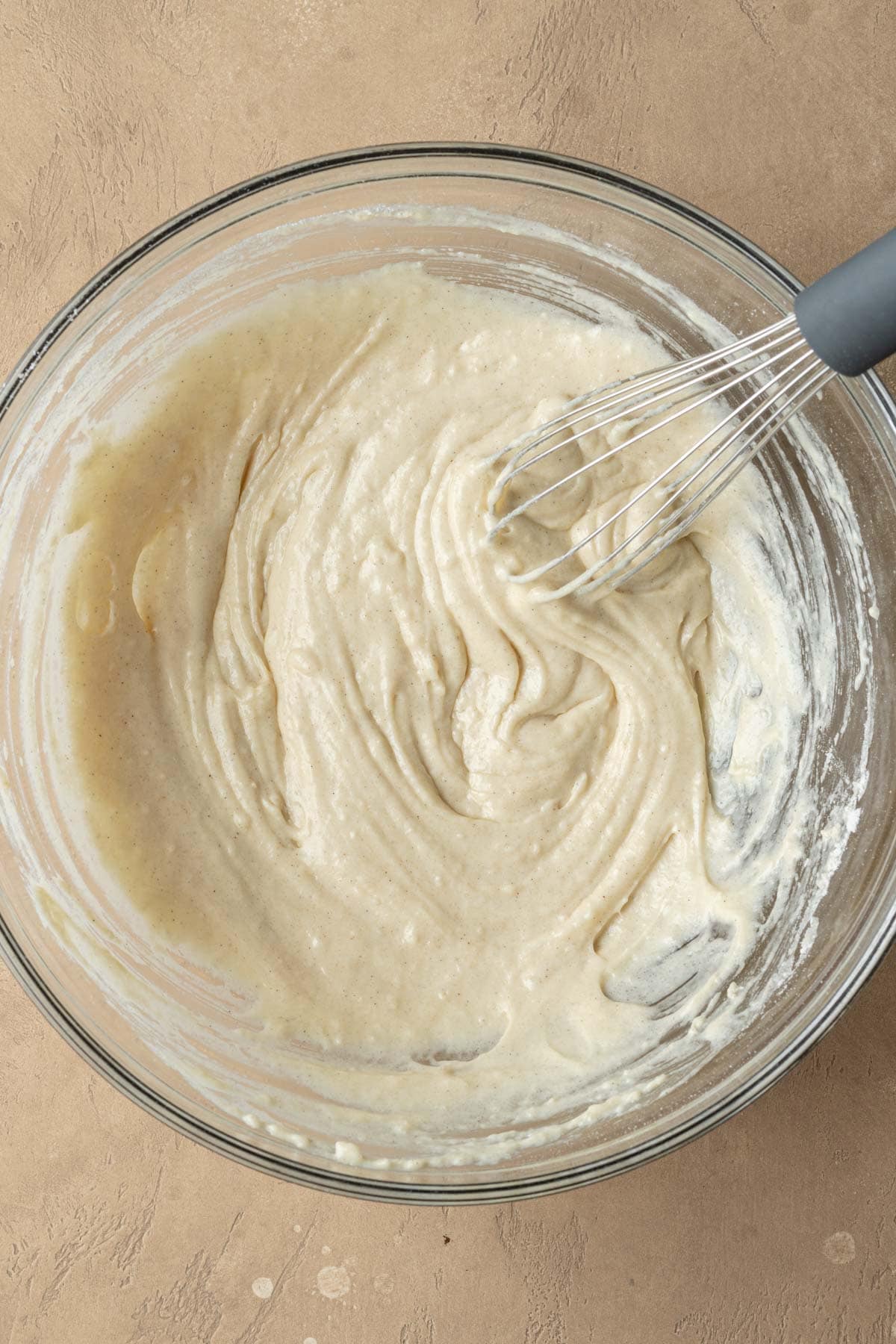 A wire whisk mixing buttermilk donut batter in a glass bowl.