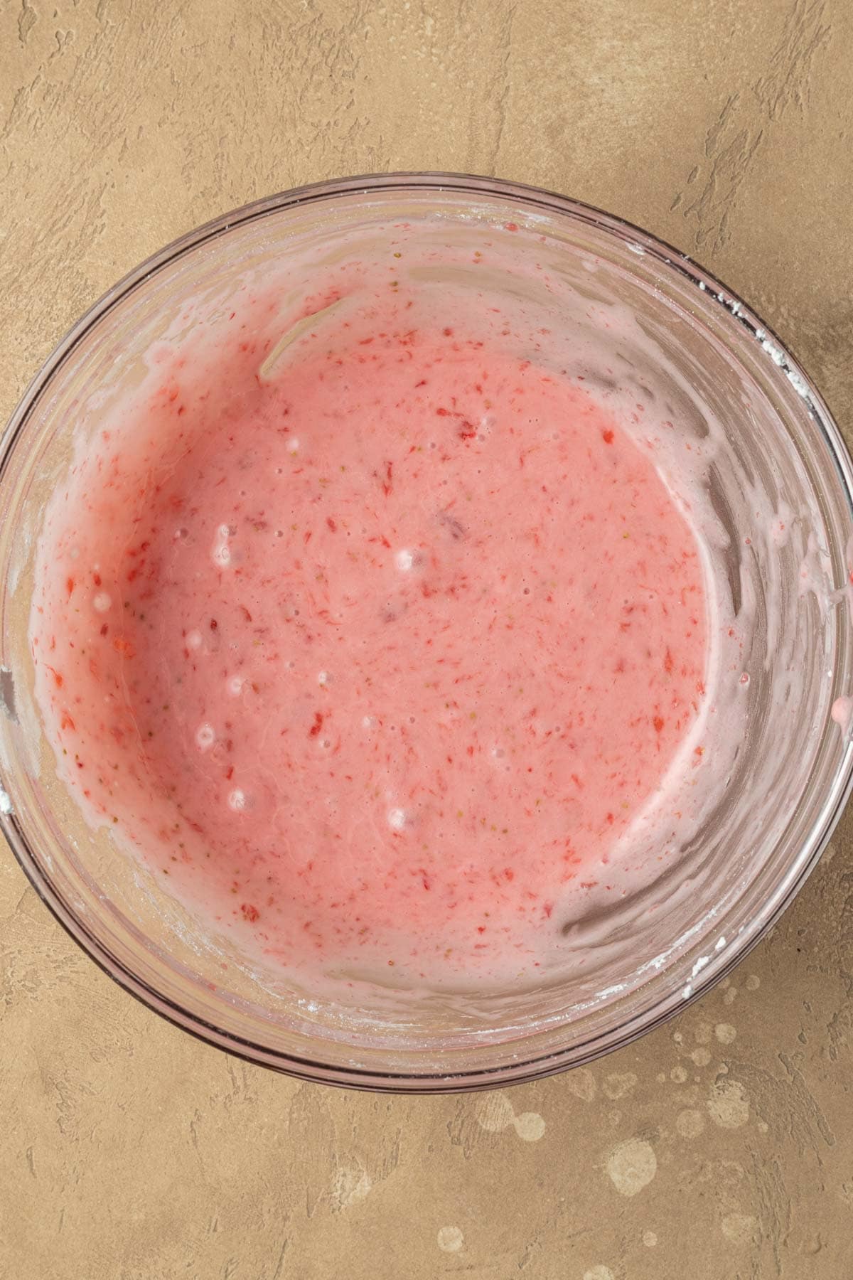 A glass bowl filled with pink strawberry glazed donut icing.