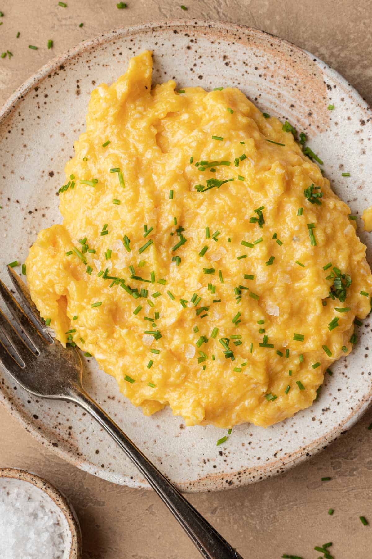 Freshly plated cheesy scrambled eggs that have fresh chives sprinkled on top!