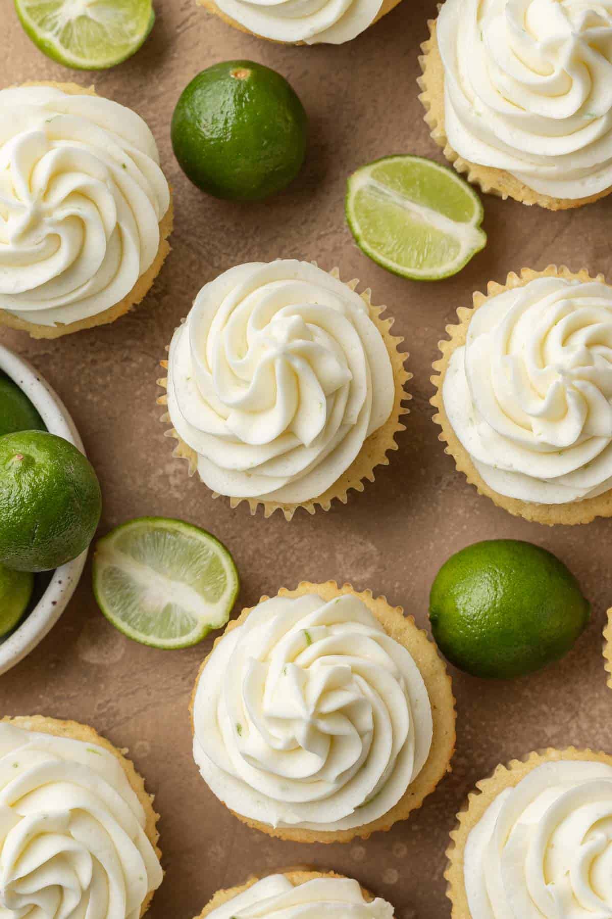 overhead view of key lime cupcakes laid out on a brown backdrop with key limes cut in half. 