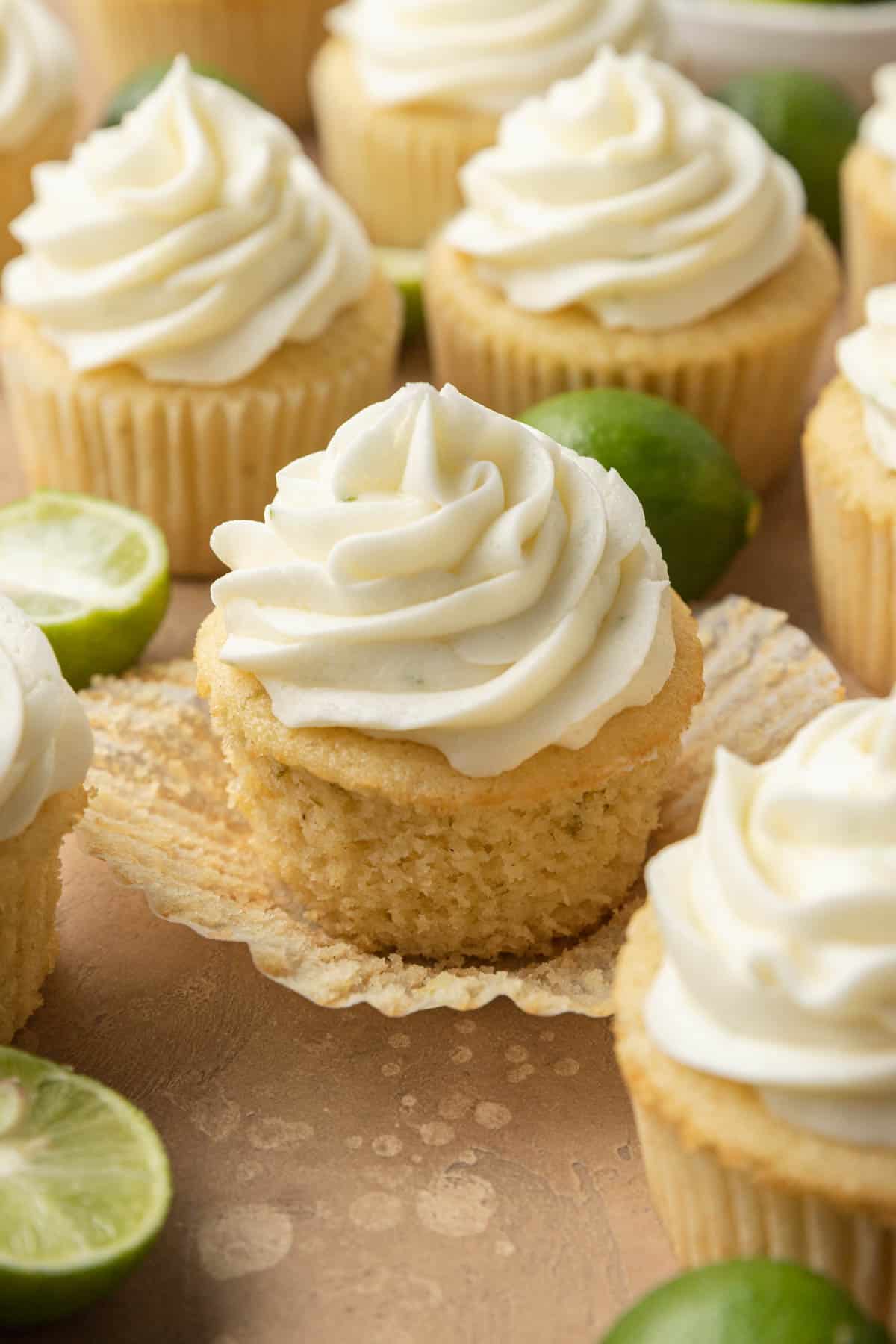 A key lime cupcake on a wrapper surrounded key other cupcakes and little key limes. 