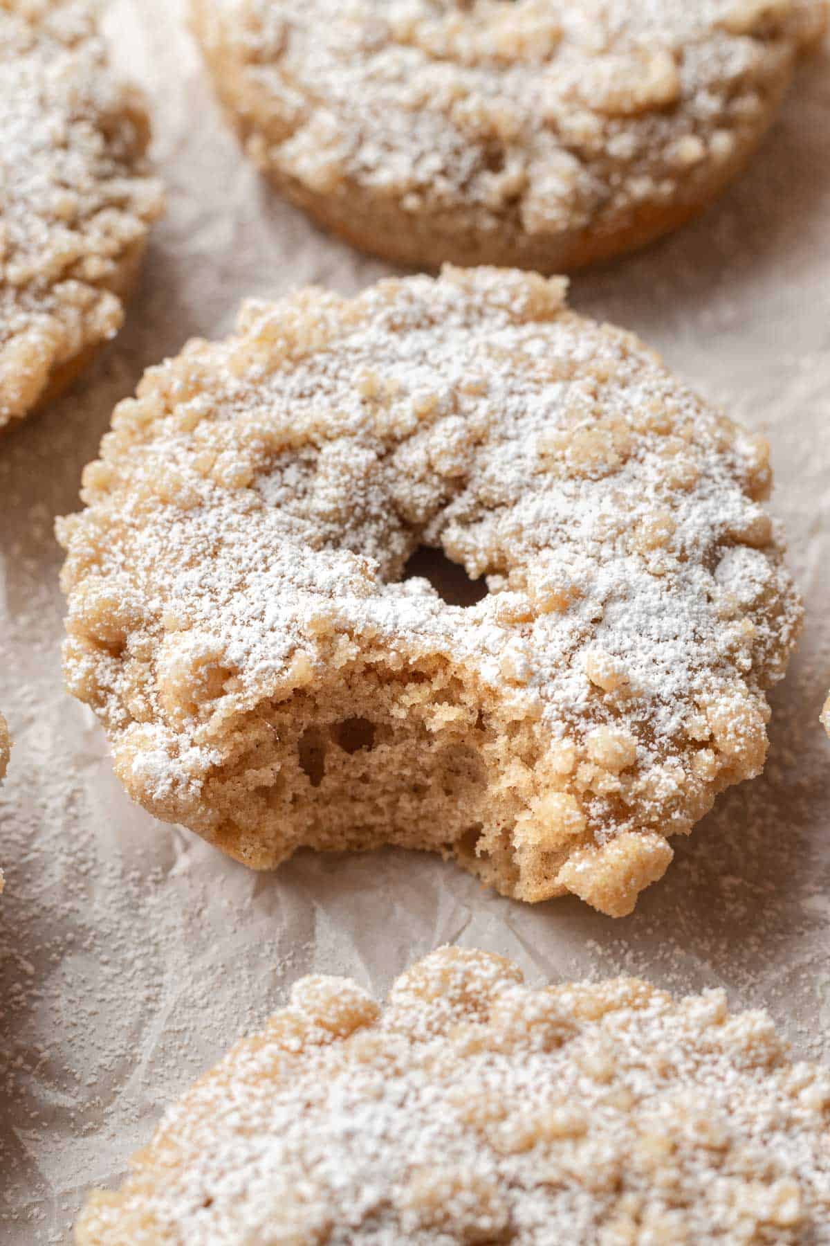Close up image of a crumb donut resting on a baking sheet and topped with powder sugar.