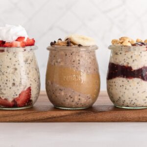 3 jars of different flavored overnight oats on a wooden board with toppings on each.
