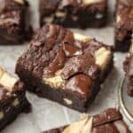 triple chocolate brownie square on white parchment paper surrounded by other brownies.