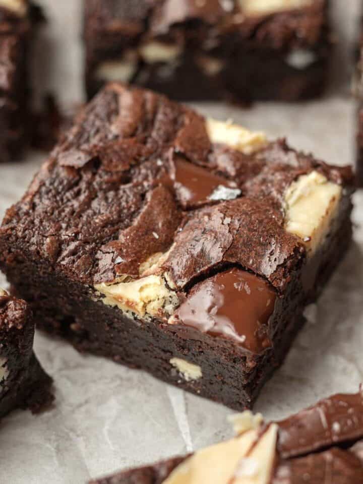 triple chocolate brownie square on white parchment paper surrounded by other brownies.