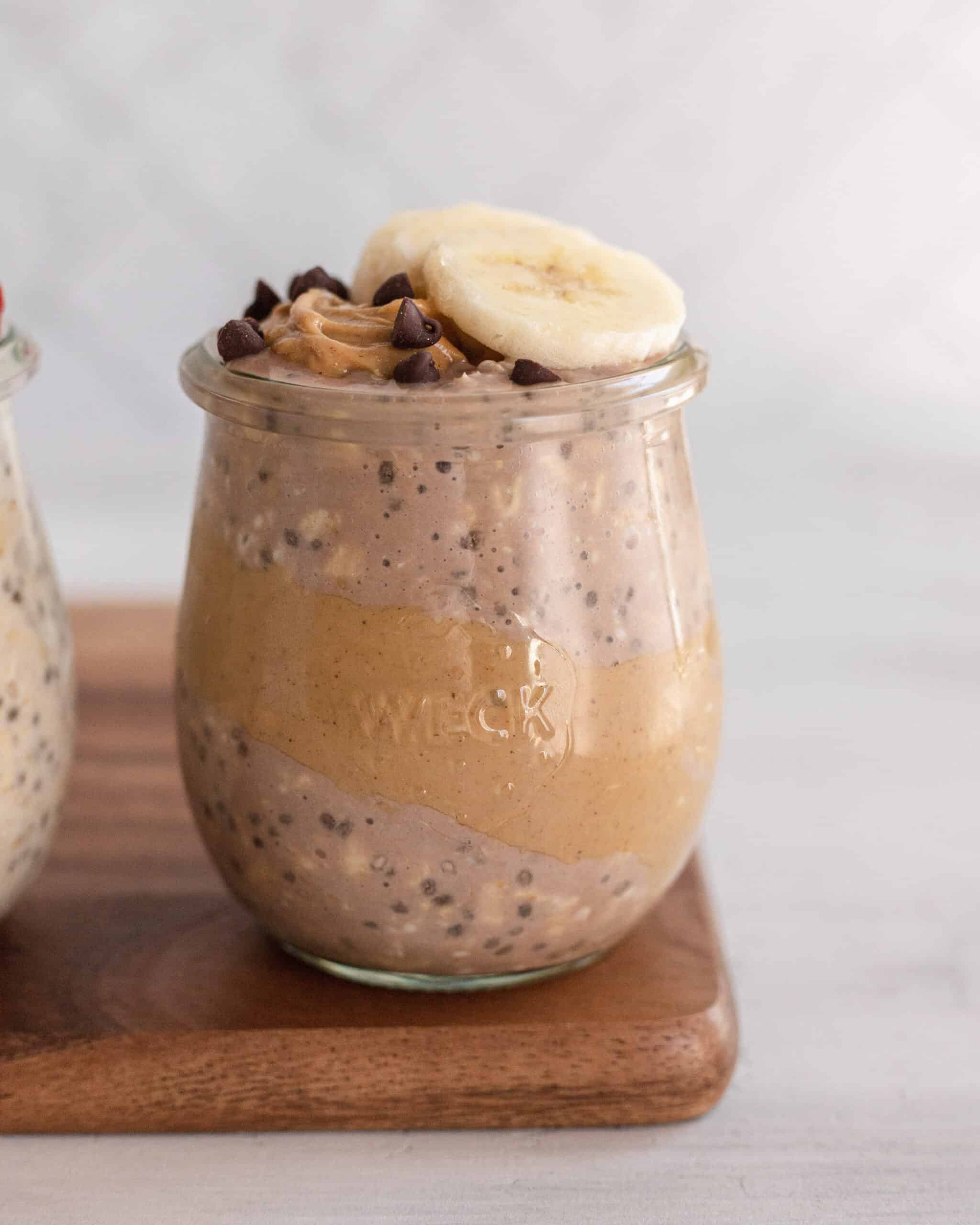 clear glass jar with chocolate overnight oats and a strip of peanut butter on the jar, topped with banana and mini chocolate chips
