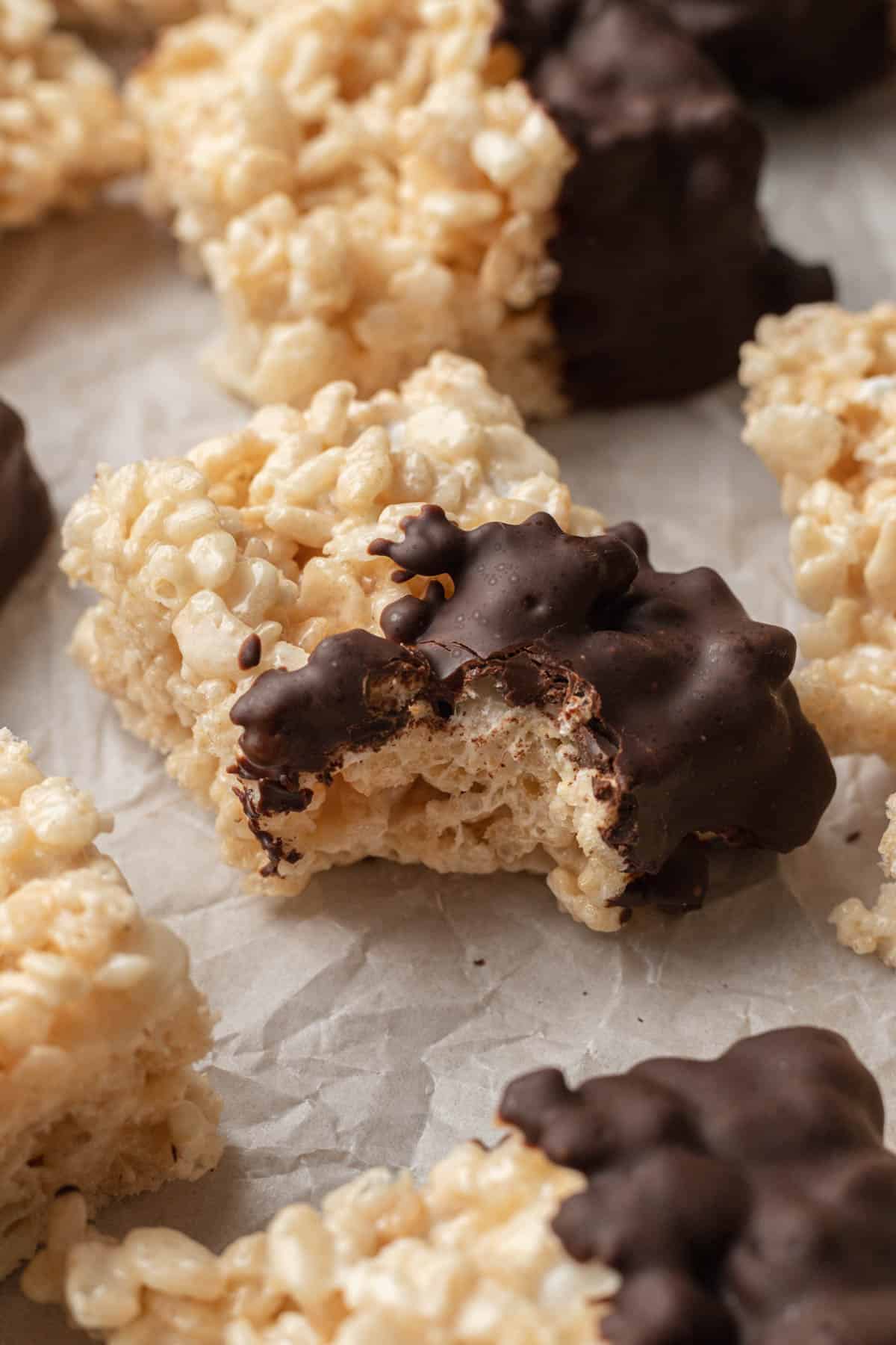 Fresh batch of chocolate dipped rice krispie treats on parchment paper with a bite taken out of it.