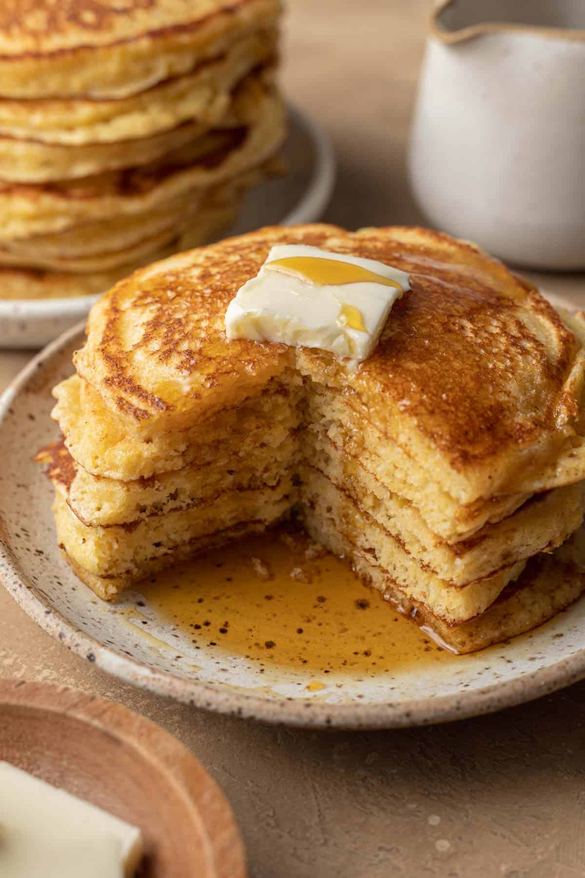 Stake of cornbread pancakes with a chunk missing. Topped with butter and syrup.