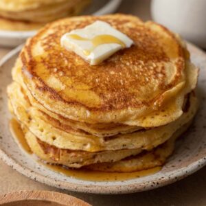 Fresh stack of cornbread pancakes plated with butter and syrup on top.