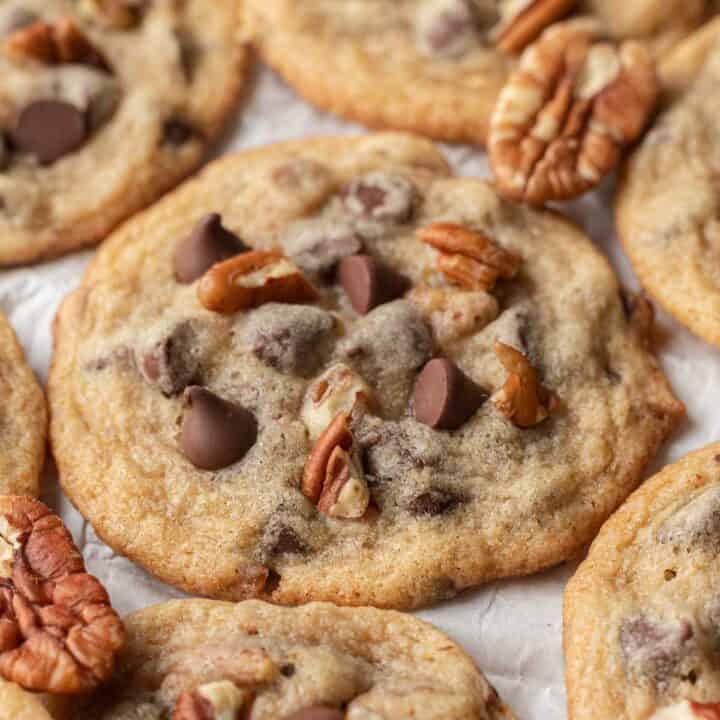 Close up image of a fresh batch of pecan chocolate chip cookies laying out on parchment paper.