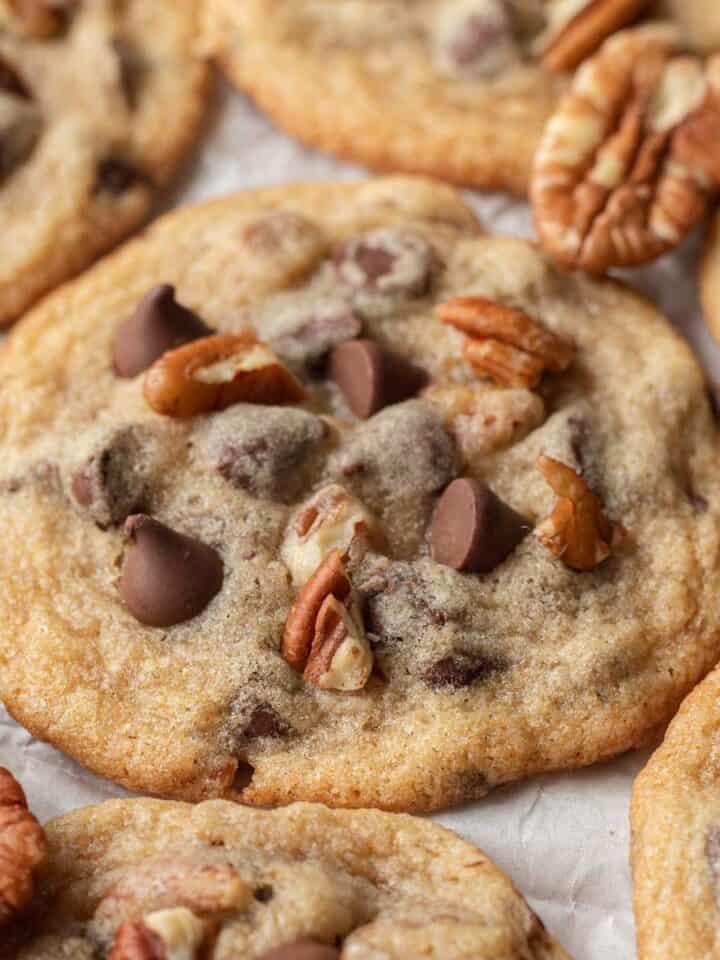 Close up image of a fresh batch of pecan chocolate chip cookies laying out on parchment paper.
