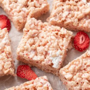 strawberry rice krispie treats squares on white parchment paper surrounded by freeze dried strawberries