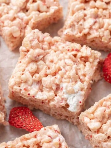 strawberry rice krispie treats squares on white parchment paper surrounded by freeze dried strawberries