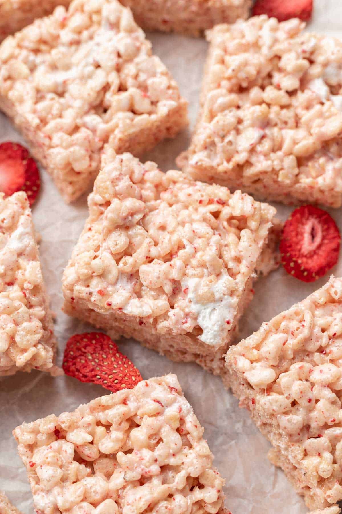 freshly made strawberry rice krispie treats sitting on parchment paper with freezer dried strawberries.
