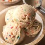 Freshly scooped balls of edibale sugar cookie dough sitting in a wooden bowl.