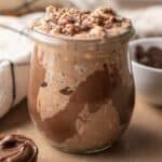 Close up shot of a freshly made jar of nutella overnight oats topped with nutella drizzle.