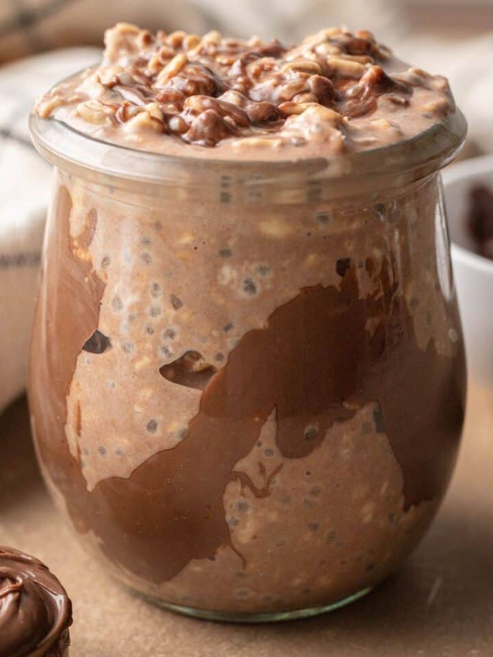 Close up shot of a freshly made jar of nutella overnight oats topped with nutella drizzle.
