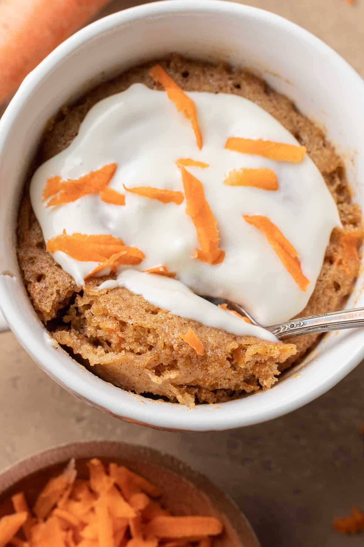 Birds eye view of a carrot cake mug cake that has frosting on top with shredded carrots sprinkled over the mug cake.