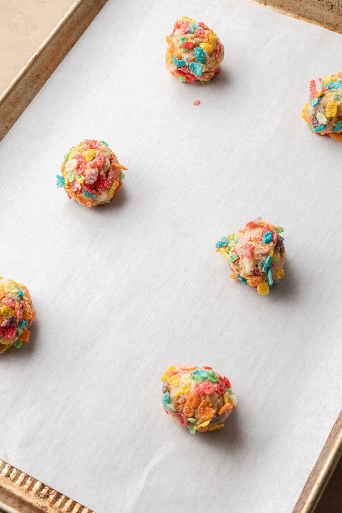 fruity pebble cookies rolled in fruity pebble cereal on a baking sheet